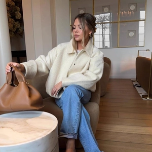 Women's warm beige sherpa jacket with blue high-waist jeans and a caramel leather tote bag