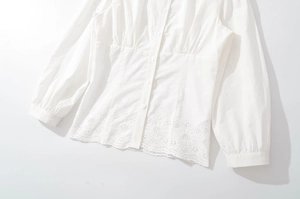 Détail de chemise blanche à manches longues avec broderie ajourée et taille plissée