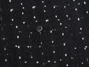Makro-Detail von schwarz-weißem Tweed-Stoff mit einem silbernen, runden Knopf-Element