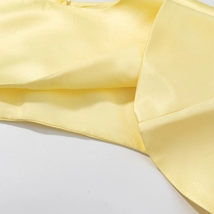 Détail du tissu satiné jaune pâle montrant un lustre soyeux de qualité et des coutures