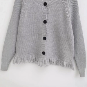 Gray knit cardigan featuring button closure and long fringe hem on a white background