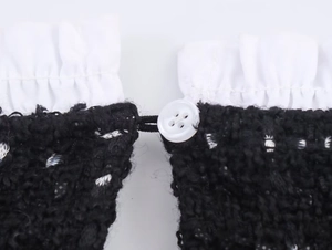 Detail eines Tweedkleides mit Rüschenbesatz und weißem Knopfverschluss mit Kordelschlaufe