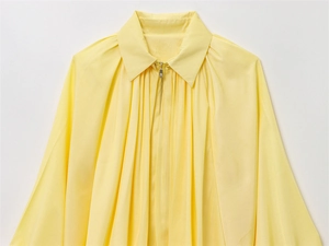 Détail de veste plissée jaune clair avec col pointu classique et fermeture éclair en métal