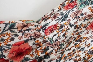 Dettaglio del ricamo a punto smock floreale e trama plissettata elastica del vestito