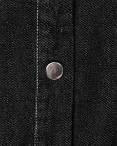 Detail of black denim fabric with silver metal snap button and white contrast stitching