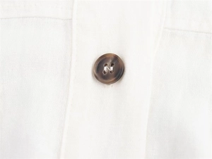 Detail of white cotton linen fabric and brown tortoiseshell button on a midi dress