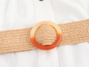Detailed close-up of woven straw belt with a gradient resin ring buckle on white fabric