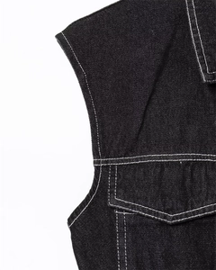 Detailed close-up of black denim vest with contrast white stitching and flap pocket