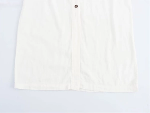 Detailed close-up of white cotton linen shirt dress hem with brown tortoiseshell button