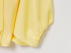 Gros plan sur les poignets plissés et la texture mate de la veste bomber jaune clair