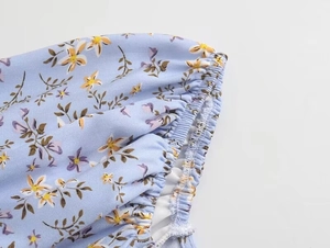 Détail de robe fleurie bleu clair avec poignets élastiques à volants et coutures précises