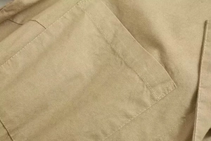 Detail of a square patch pocket on light beige linen fabric with clean stitching