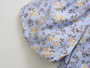 Gros plan sur la robe à fleurs bleu clair montrant l'imprimé marguerites et le plissé