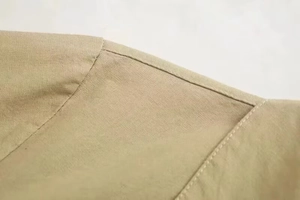 Close-up of double-stitched seams and textured linen fabric on a khaki jumpsuit