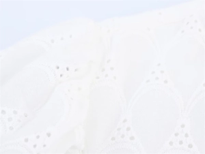 Close-up of white eyelet lace embroidery fabric with delicate wave patterns