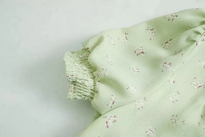 Detail eines hellgrünen floralen Chiffonkleides mit elastischen Manschetten und Stoffstruktur