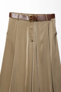 Detail view of champagne satin wide-leg trousers with elegant pleats and leather belt