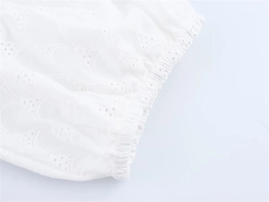 Detail of white embroidered eyelet fabric with intricate hollow patterns and elastic cuffs