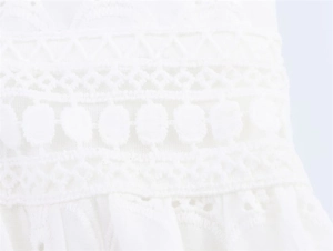 Macro detail of white embroidery lace fabric with geometric cutouts and pom-pom trim