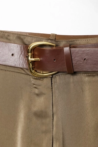 Detail of high-waist satin trousers with glossy fabric and a gold buckle belt