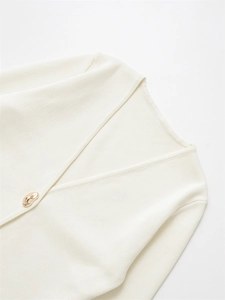 Close-up of cream knit cardigan featuring a decorative irregular gold button and V-neckline