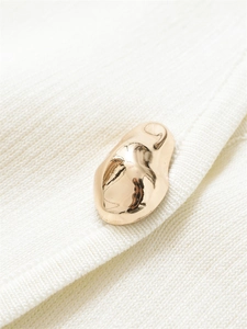 Macro detail of high-shine gold asymmetric metal button on premium white knit cardigan fabric
