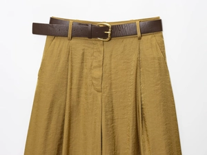 Detail of high-waist mustard satin wide-leg trousers with brown belt and gold buckle