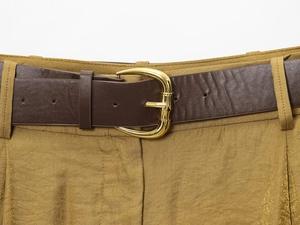 Detail of dark brown leather belt with golden horseshoe buckle on yellow trousers