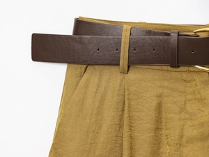 Detail of mustard yellow pleated trousers with metallic fibers and brown leather belt