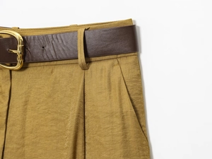 Detail of high-waist satin trousers featuring a brown leather belt and golden metal buckle