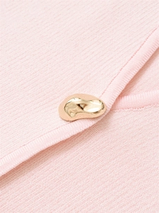 Detail of light pink knit fabric texture featuring a decorative irregular gold metal button