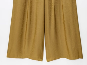 Detail of gold satin wide-leg trousers showing metallic texture and pleated fabric