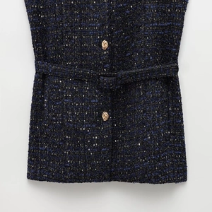 Detail of tweed fabric vest with sequins, gold embossed button and matching waist belt