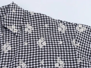 Detail of white daisy embroidery on black and white gingham shirt with lapel collar