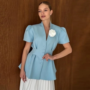 Détail d'un blazer bleu clair à manches courtes avec une fleur rose 3D blanche et taille