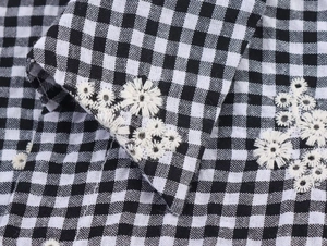 Close-up of intricate white daisy embroidery on black and white gingham check fabric