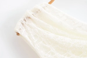 Close-up detail of white hollow lace fabric with intricate floral patterns on a hanger