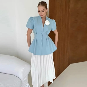 Détail d'un blazer bleu clair à basque avec une broche fleurie blanche tridimensionnelle