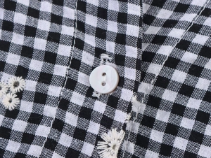 Macro detail of gingham fabric with daisy embroidery and a white button fastening