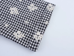 Close-up of black and white gingham fabric with detailed 3D white daisy floral embroidery