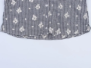 Close-up of gingham shirt hem featuring delicate flower embroidery and white buttons
