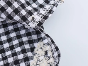 Close-up of black and white plaid fabric with delicate white daisy floral embroidery