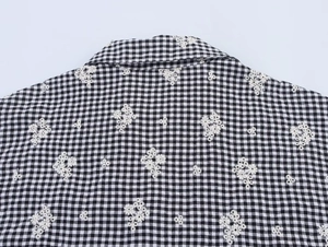 Detail of gingham shirt collar with white daisy embroidery and neat stitching texture