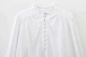 Close-up of ruffled high neck and fabric buttons on white cotton puff sleeve shirt