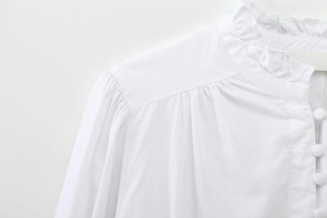 Detail of ruffled stand collar and fabric covered buttons on a white cotton blouse