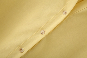Detailed close-up of linen blend fabric texture and marble-patterned buttons on yellow shirt
