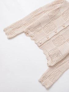 Détail du cardigan en maille beige avec motifs ajourés et finition bord festonné