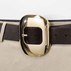 Women's dark brown leather belt with large oval gold buckle on beige trousers