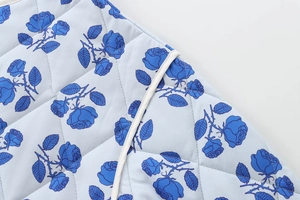 Detail of diamond-quilted fabric with blue rose floral print and white piping trim