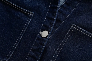 Macro shot of dark blue denim fabric with white contrast stitching and a metal button
